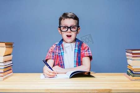 小男生在教室的课桌前学习作业。戴眼镜的学生获得知识。男生学作业，教育理念