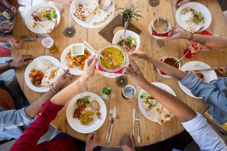 正餐美食摄影照片_休闲、美食和人的概念-一群快乐的国际朋友在餐厅的餐桌上吃饭。国际友人在餐厅用餐