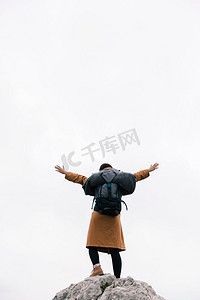 后视图妇女站在山顶提高她的手臂反对天空
