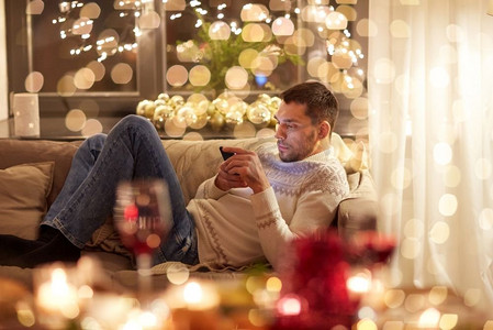 圣诞节，技术和假日概念—人与智能手机短信在家里。圣诞节期间，男子带智能手机在家