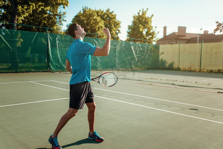 在户外球场上拿着网球拍的男人。夏季活跃的体育比赛。快乐休闲