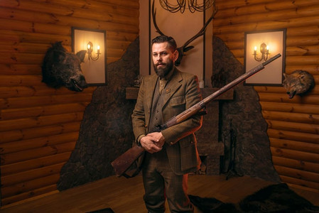 传统狩猎服装的猎人绅士用旧枪对着壁炉.