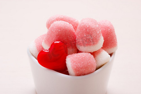 甜食糖果。粉红色果冻或棉花糖与糖在白色碗木桌上装饰有红心爱的象征