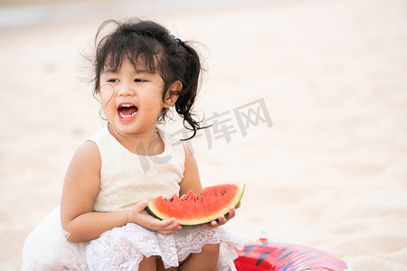 可爱的孩子吃西瓜在热带沙滩在夏天。可爱的孩子在沙滩上吃西瓜。