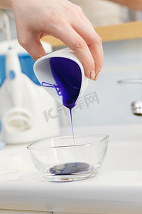 妇女倒紫色染发剂或洗发水到白色碗。卫生用品概念妇女倒紫色染发剂或洗发水