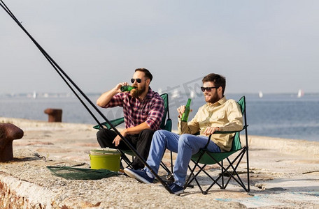 休闲与人的概念-快乐的男性朋友在码头钓鱼和喝啤酒。男性朋友在码头钓鱼和喝啤酒