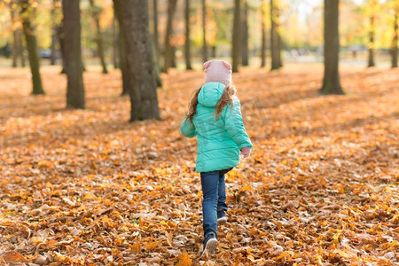 快乐的女孩秋天摄影照片_童年，季节和自然概念—快乐的女孩运行在秋天公园。快乐的女孩运行在秋天公园