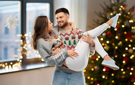 圣诞节，人们和节日的概念-幸福的情侣在丑陋的毛衣派对上超过家庭房间的背景。圣诞丑陋毛衣派对上的幸福情侣