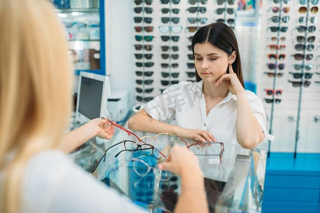女性眼镜师和女性在眼镜店选择眼镜框。由专业验光师选配眼镜