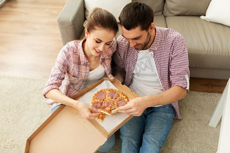 共享妻子辣文摄影照片_休闲，美食和人的概念—快乐的夫妇在家里吃外卖比萨饼。一对夫妇在家里吃外卖披萨