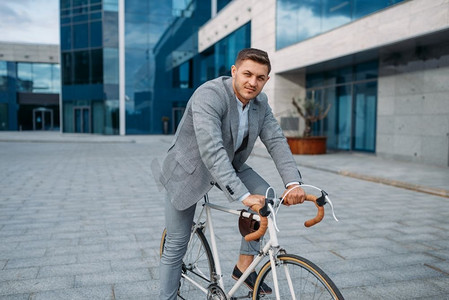 市中心，一位西装革履的年轻商人骑着自行车。商家在城市街道上乘坐生态交通工具