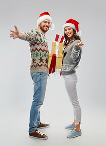人们和节日的概念-在丑陋的毛线派对上，戴着圣诞帽的幸福夫妇带着圣诞礼物。穿着圣诞毛衣送礼物的幸福小两口