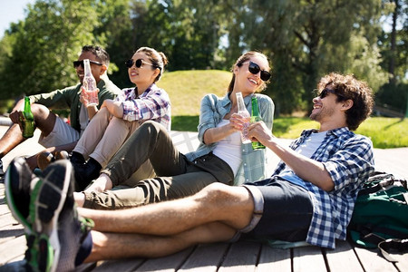 朋友的酒摄影照片_休闲，野餐和人的概念—朋友喝啤酒和苹果酒在木露台在夏季公园。朋友喝啤酒和苹果酒在夏季公园