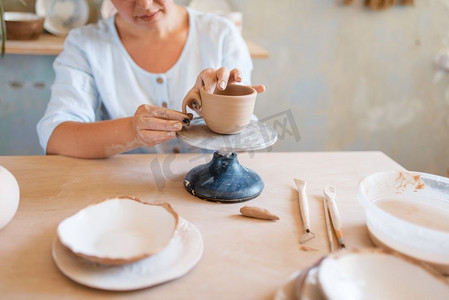 陶瓷工艺摄影照片_女陶工皮壶、制陶车间。女人塑造一个碗。手工陶艺，粘土餐具。女陶工皮壶、陶作坊
