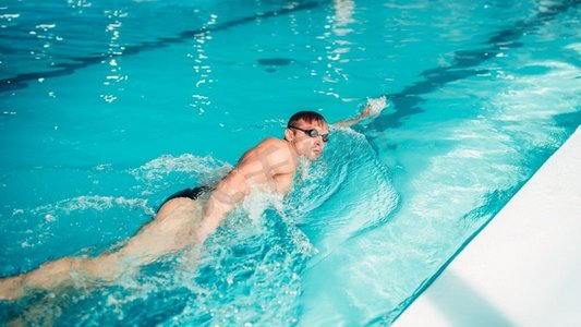 蝶泳摄影照片_游泳运动员戴眼镜在蝶泳式，室内游泳池。竞技游泳运动员以蝶泳的方式游泳