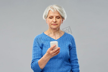 技术和老年人概念—高级妇女使用智能手机在灰色背景。使用智能手机的老年妇女