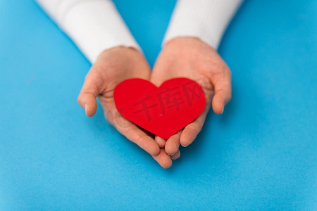 爱情、健康和情人节S日概念-手持红色心形，蓝色背景。蓝色背景上手持红色心形