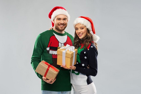 人们和节日的概念-在丑陋的毛线派对上，戴着圣诞帽的幸福夫妇带着圣诞礼物。穿着圣诞毛衣送礼物的幸福小两口