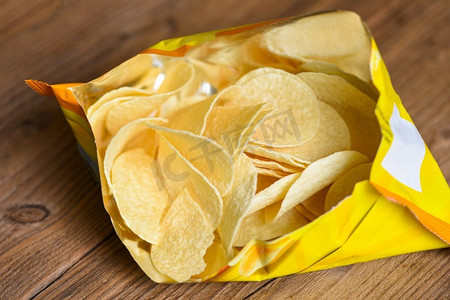 反塑料包装摄影照片_土豆片的木质背景，土豆片是袋装的零食，用塑料包装即食，还有脂肪食品或垃圾食品