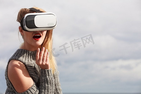 一名年轻女子在外面测试VR眼镜。女性在春天的天气里戴着虚拟现实耳机。戴着VR的女人在外面