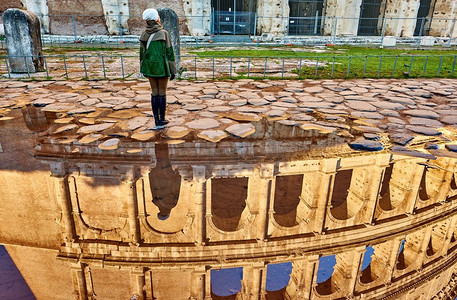 妇女游客在鹅卵石砖铺湿街道与斗兽场反射在罗马，意大利
