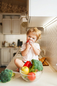 小女孩坐在桌子上吃西红柿。女宝宝从厨房里的碗里品尝蔬菜。儿童品尝素食