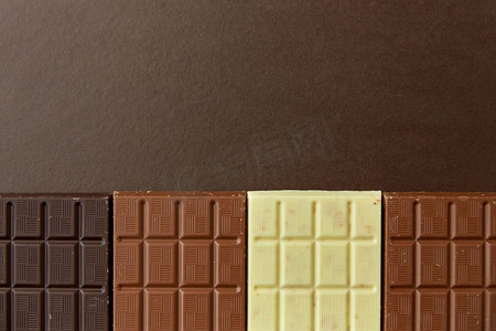 糖果，糖果和食物概念—牛奶，黑和白巧克力棒在棕色背景。不同种类的巧克力在棕色背景