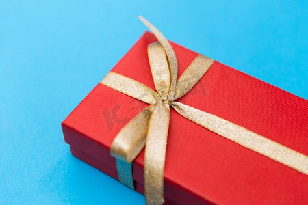 节日，问候和惊喜概念-圣诞红色礼盒，蓝底金色蝴蝶结。蓝色背景的圣诞红色礼盒