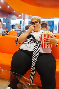 胖女人拿着爆米花在电影厅，不健康的垃圾食品。商场里超重的女性，肥胖问题
