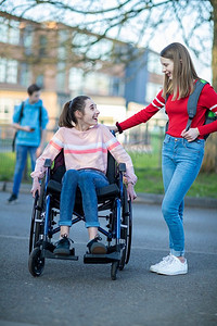 十几岁的女孩在轮椅上与朋友交谈，因为他们离开高中