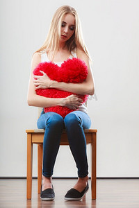 心碎的爱情概念。悲伤的不快乐的女人坐在椅子上拥抱红心枕头