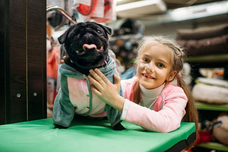 小女孩和有趣的小狗在衣服，宠物店。宠物店里的小孩和狗，家畜用品