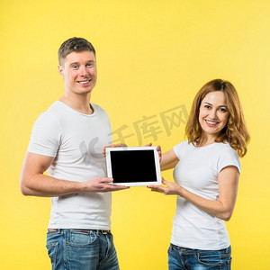 肖像两个快乐的年轻夫妇显示黑色屏幕数字平板电脑反对黄色背景