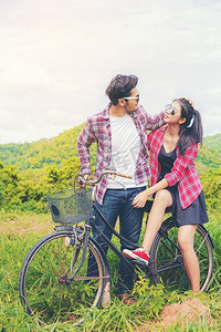 幸福的一对年轻男女在山上绿草如茵的草地上骑自行车。热爱和旅行的生活方式理念。