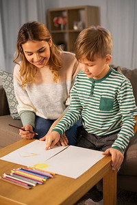 孩子彩色铅笔摄影照片_家庭，休闲和人的概念—母亲和小儿子与彩色铅笔和纸提请在家里。母亲和儿子与铅笔绘画在家里
