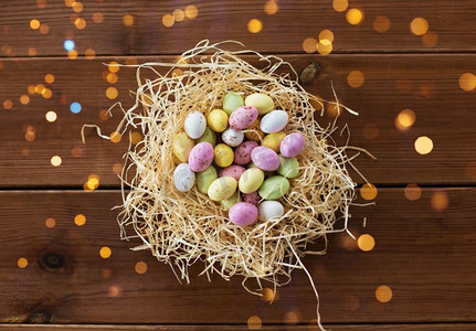 复活节，糖果和假日概念—糖果下降蛋在稻草巢在木背景复活节彩蛋在稻草巢在木桌