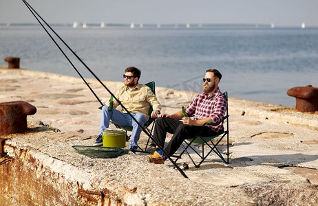 休闲与人的概念-快乐的朋友在码头钓鱼和喝啤酒。快乐的朋友们在码头钓鱼和喝啤酒
