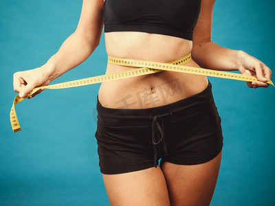 减肥，苗条身材，健康生活理念。适合健身女孩测量她的腰围与测量磁带在蓝色