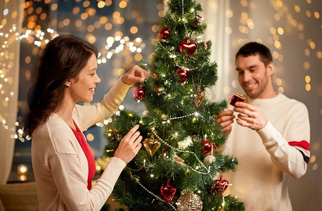寒假摄影照片_寒假和人们概念快乐的夫妻在家中装饰圣诞树。幸福的夫妻在家中装饰圣诞树