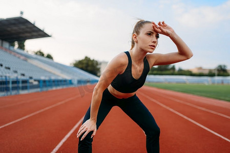女性疲惫摄影照片_疲惫的女慢跑者穿着运动服，在体育场训练。女性在户外竞技场跑步前做伸展运动