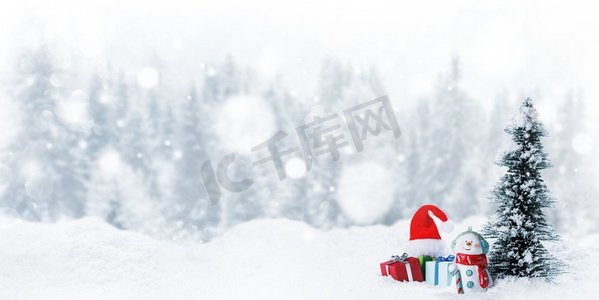 雪人在雪地上放着冷杉树和圣诞礼物雪橇，冬天的森林和白色的雪花落在雪地上。雪人和圣诞装饰品
