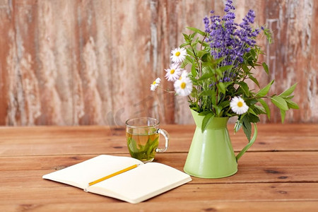 生态和有机概念-草药茶，桌上有带铅笔和绿色罐子里的花的笔记本。餐桌上的罐装凉茶、笔记本和鲜花