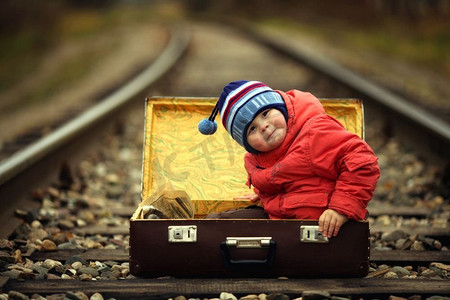 坐在火车路程附近的行李箱里的男孩