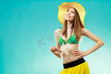 比基尼摄影照片_暑假概念。特写镜头妇女在黄色帽子比基尼拿着白色壳海星在生动的蓝色背景的手