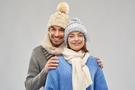 人，圣诞节和冬天衣服概念—在灰色背景的编织帽子和围巾的愉快夫妇快乐的夫妇在冬天的衣服