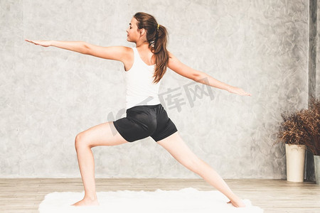 年轻漂亮的女人做瑜伽练习在地毯在家里客厅。健康的生活方式和放松。