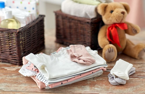 婴儿时代和服装概念—婴儿衣服，泰迪熊玩具和篮子在木桌子在家里。婴儿衣服和泰迪熊玩具在桌子上在家里