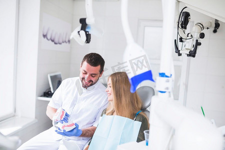 显示牙齿模型患者的愉快的男性牙医室内一角人物特写