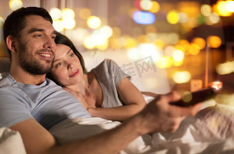人、家、闲理念--幸福夫妻晚上在家床上看电视。幸福的夫妻晚上在家床上看电视