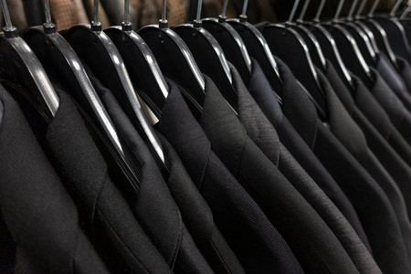 男士在商店、衣柜或壁橱栏杆的衣架上挂着黑色、灰色和蓝色的深色西装